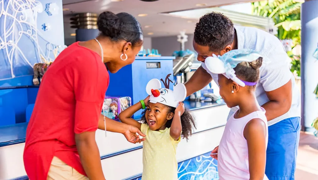 Little girl excited about her Olaf character hat with family at a Disney park merchandise stand.