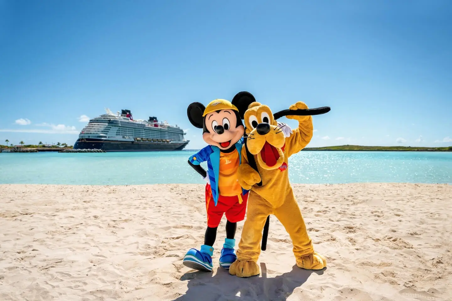 Mickey Mouse and Pluto posing on a beach with a Disney cruise ship behind them.