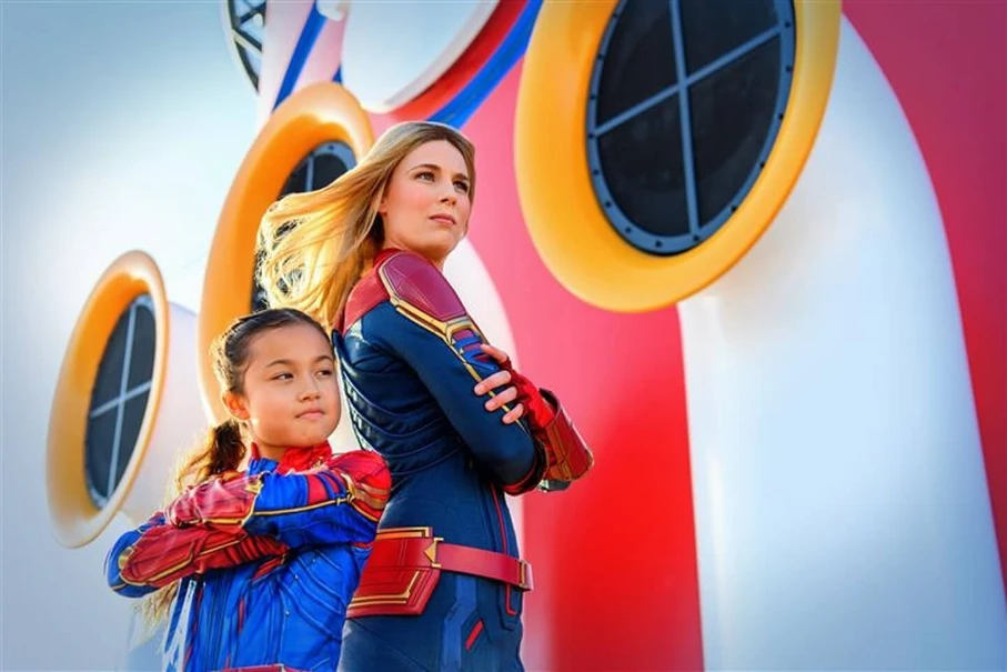 Adult and child in Captain Marvel costumes stand heroically with arms crossed on a Disney cruise ship.