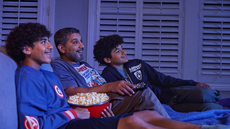 Dad and sons enjoying movie night, wearing Marvel shirts.