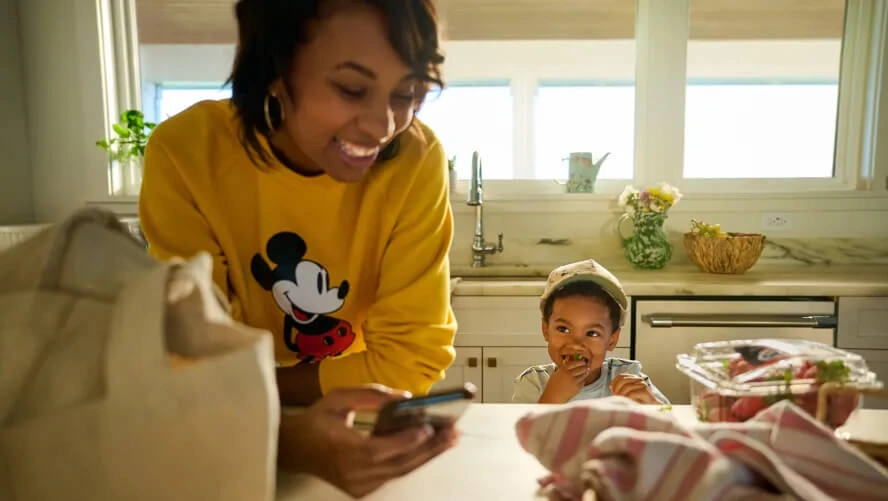 Disney mom wearing a yellow Mickey sweatshirt laughing with her son eating a snack.
