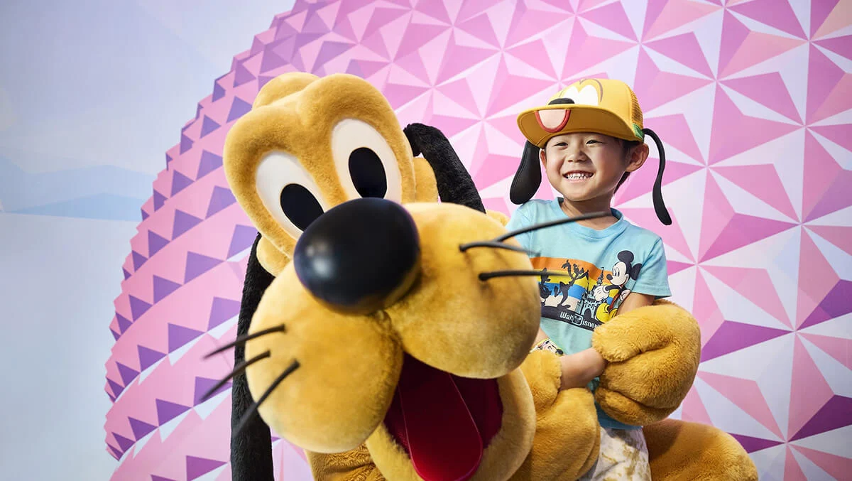 Disney's Pluto and toddler in a Mickey t-shirt smiling at Character Experience photo opportunity at EPCOT.