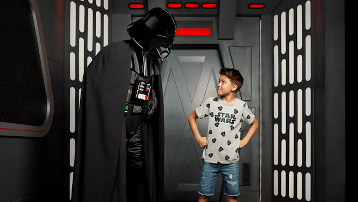 Young boy in Star Wars t-shirt standing with Darth Vader for a Disney Star Wars character experience.