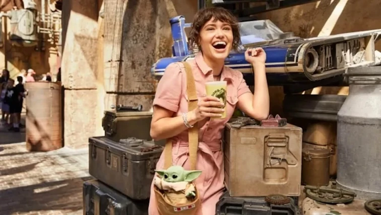 Woman holding a green milk at Star Wars: Galaxy’s Edge marketplace, with a Grogu plush in her bag.