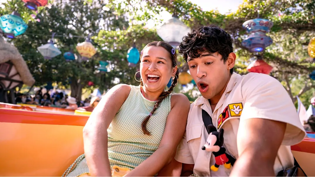 Young couple enjoying Mad Tea Party attraction at a Disneyland, with festive lanterns overhead and a Mickey Mouse plush toy.