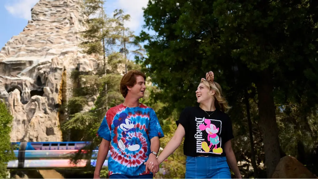 Couple wearing Mickey Mouse t-shirts near the Matterhorn and passing monorail at Disneyland Park.