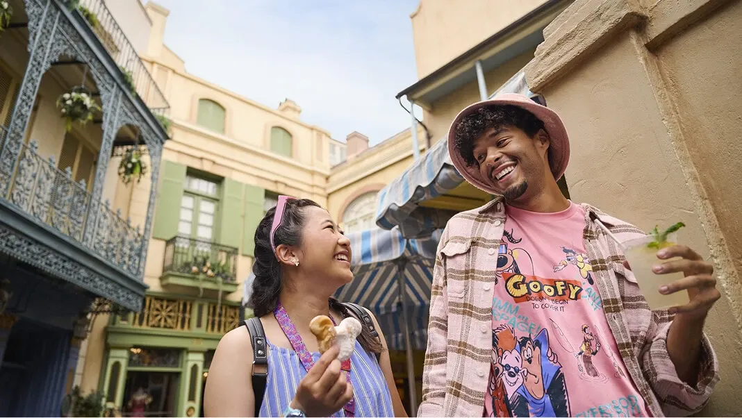 Couple enjoying Disney treats; a Mickey-shaped beignet and a mojito in New Orleans Square at Disneyland.