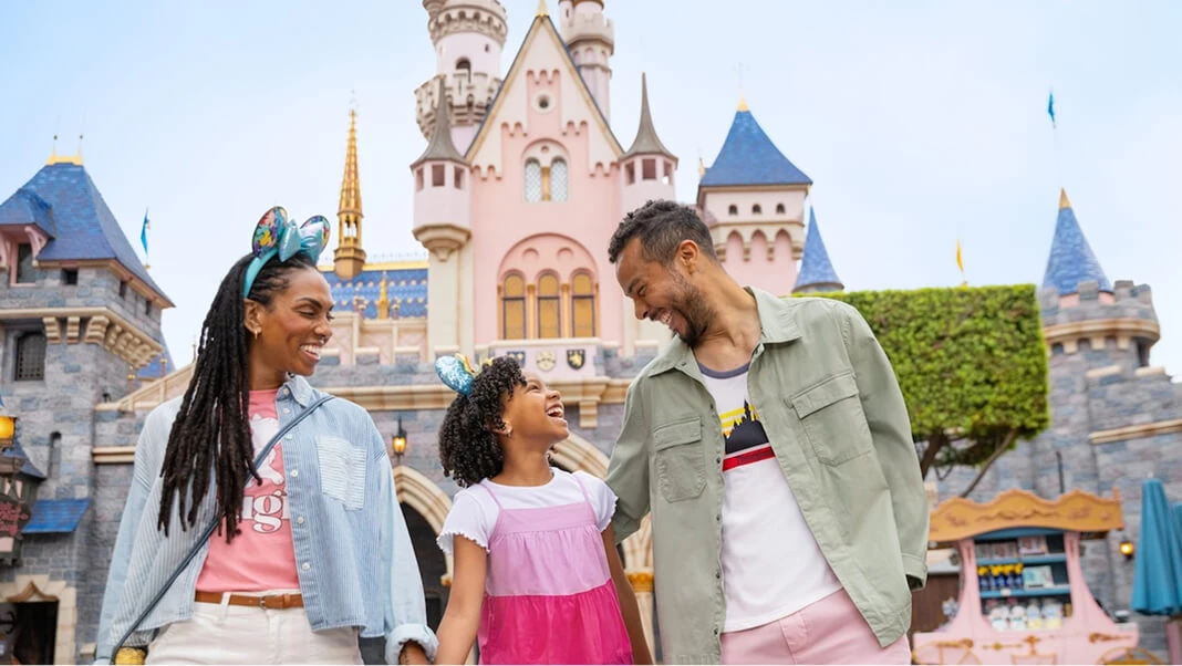 Disney family wearing Mickey Mouse ears in front of Sleeping Beauty Castle at Disneyland Park.