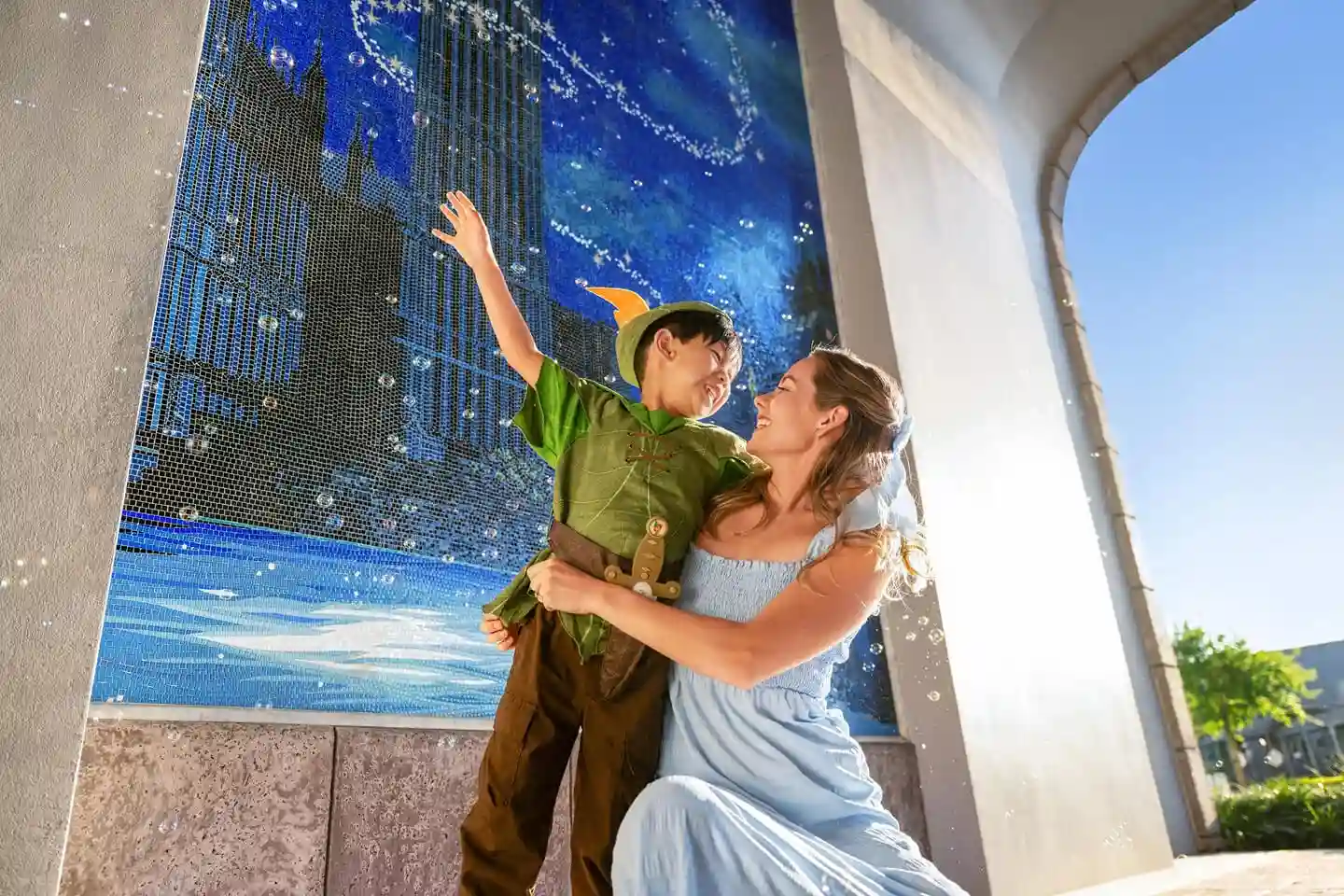 Disney mom and son in a Peter Pan outfit foreground a mural at Disney&rsquo;s Riviera Resort at Walt Disney World.