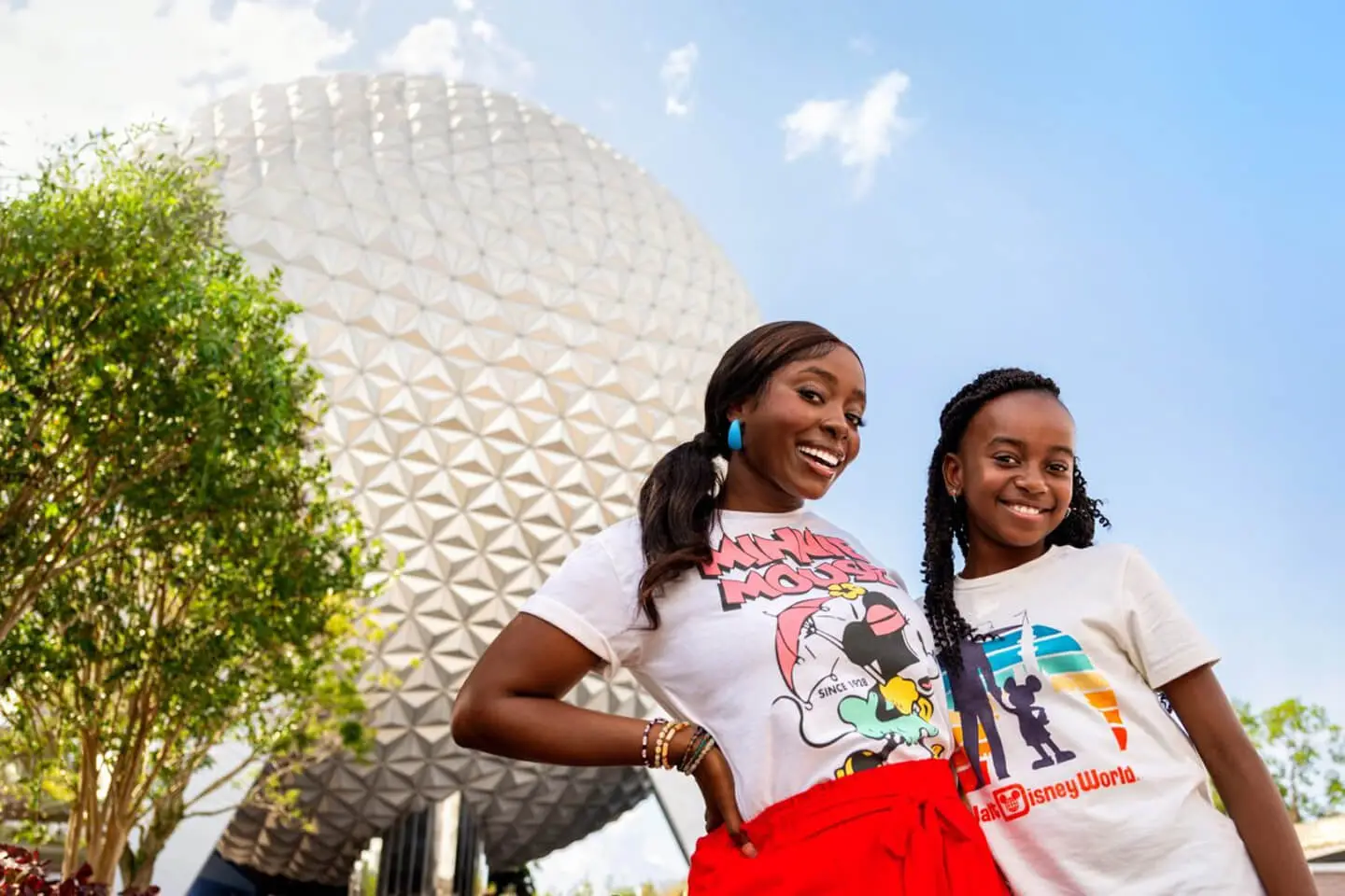 Sisters smiling in front of Spaceship Earth at EPCOT in Walt Disney World, wearing colorful Disney T-shirts.