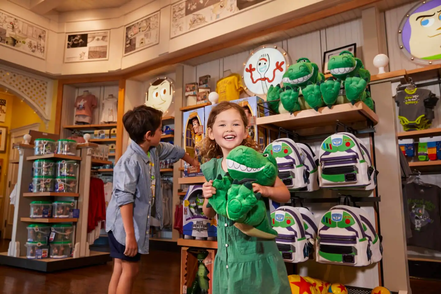 Toddler holding a Rex plush while in a Toy Story-themed store filled with Buzz Lightyear backpacks and toys.