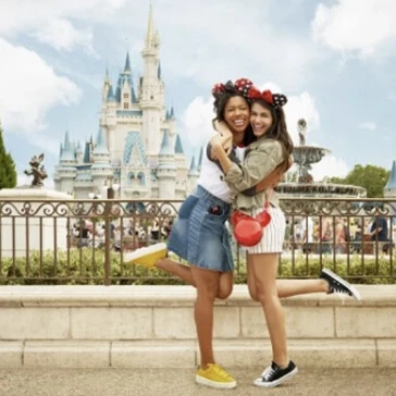 Two friends wearing Mickey ears hug in front of Cinderella Castle at Magic Kingdom.