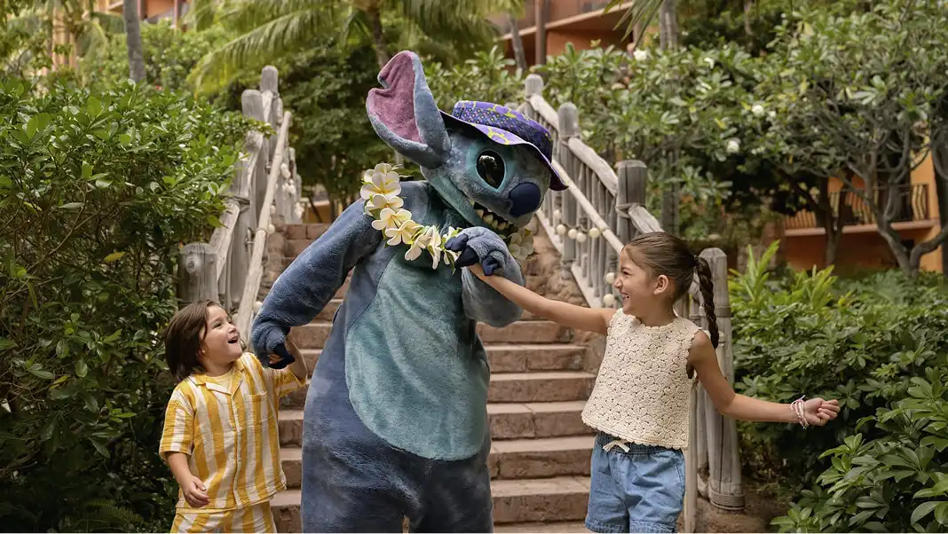 Stitch in a lei and sun hat walking with two children at Aulani, A Disney Resort & Spa in Hawaiʻi.