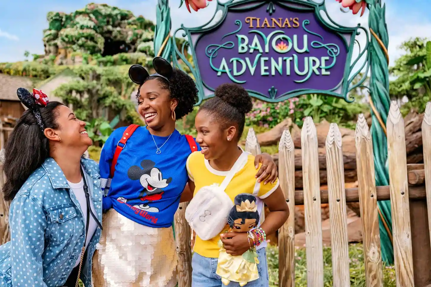 Three girls with Mickey and Minnie Mouse ears at the entrance of Tiana’s Bayou Adventure.