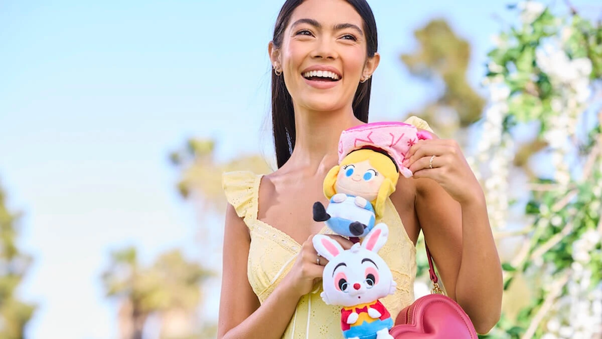 Woman smiling with Disney Alice in Wonderland mini plush toys and a heart-shaped shoulder bag.