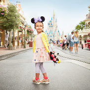 Young girl standing on Main Street holding a stuffie and wearing Minnie ears.