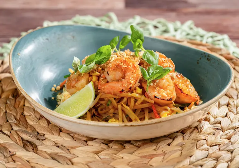 Stir-fried shrimp, tamarind sauce, toasted peanuts, crispy garlic and egg sit atop rice noodles with fresh basil