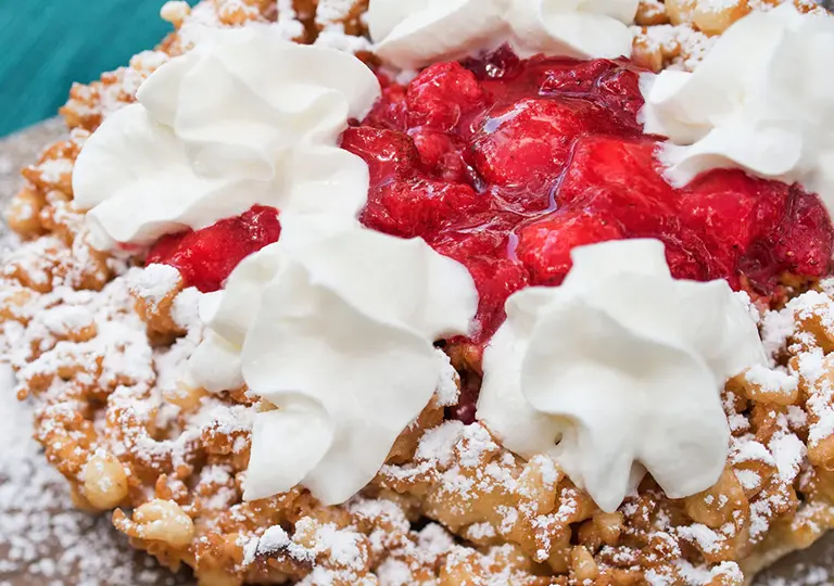 Funnel Cake topped with strawberry, powdered sugar and whipped cream.