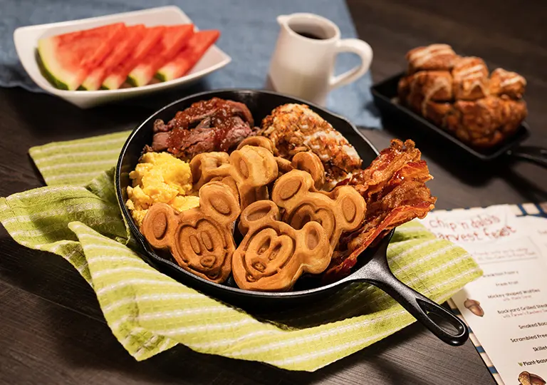 Cast iron skilled featuring the Chip N Dale Harvest Breakfast, breakfast pastries, fresh fruit, grilled steak, smoked bacon, Mickey-shaped waffles, scrambled eggs and skillet potatoes